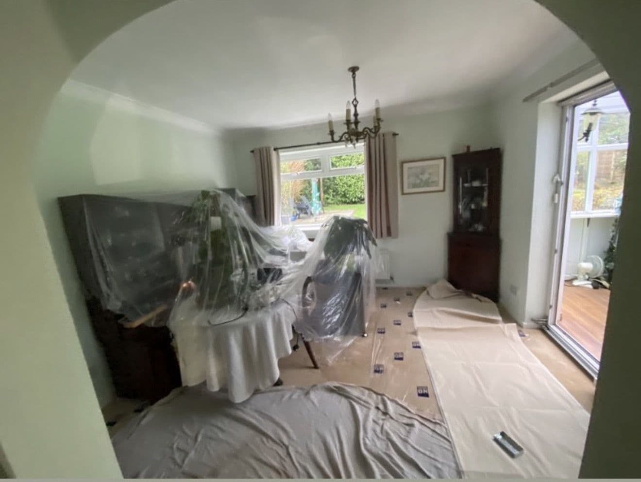 Living room ready to go: furniture pulled together, covered in plastic, dust sheets down and every wall clear - preparing a home for a house rewire